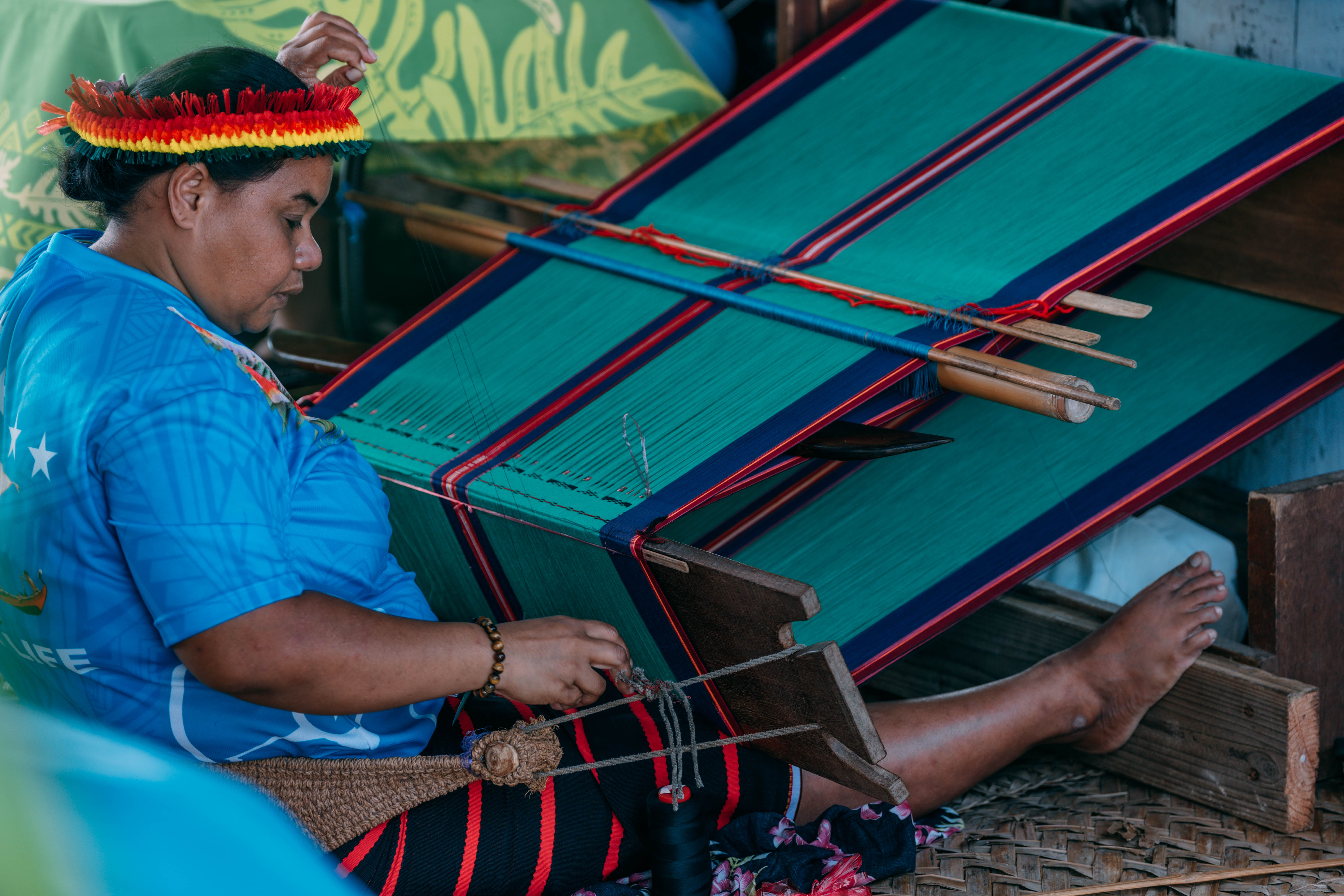 A cultural practitioner weaving a colorful textile on a loom.