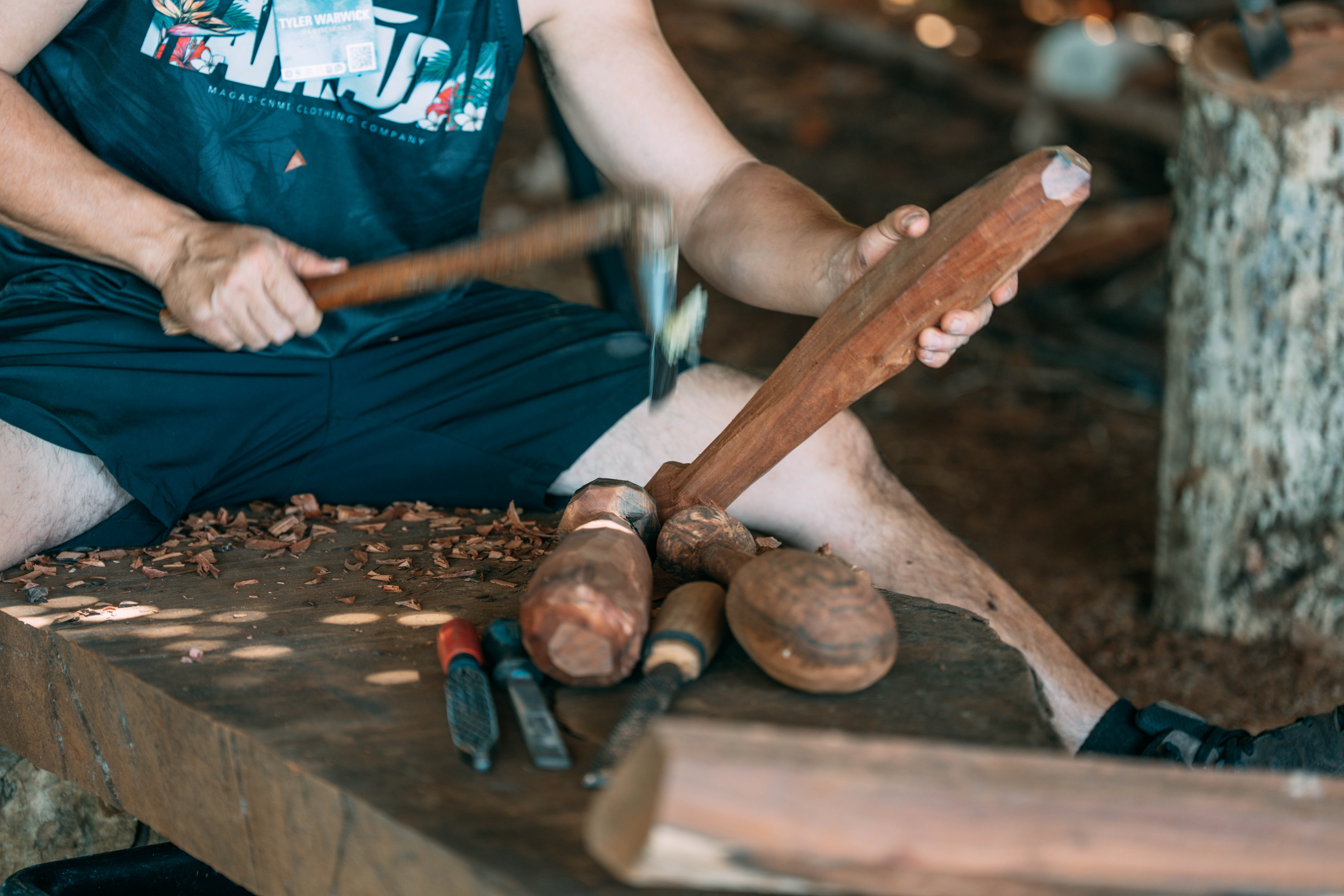 A craft artist carving a wooden cultural object with hand tools.